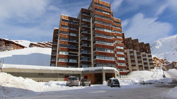 Et moderne hotel med flere etager, med altaner og en skibakke i baggrunden.