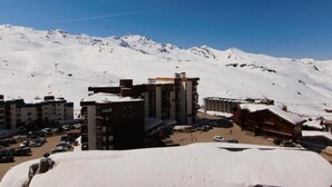 En snedækket bjergby med bygninger, heriblandt et hotel og et træhytte, og en klar blå himmel.
