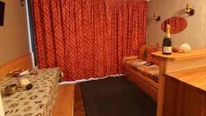 A cozy room with a wooden bed, a small table with a patterned tablecloth, a bottle of champagne, and a red curtain. - 200m from resort center, 2nd floor, balcony, tv, 21m², Val Thorens (Val Thorens)