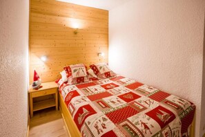 A bedroom with a wooden headboard, a quilted bedspread, and a nightstand with a lamp. - 200m from ski slopes, 1st floor, balcony, tv, 37m², Val Thorens (Val Thorens)