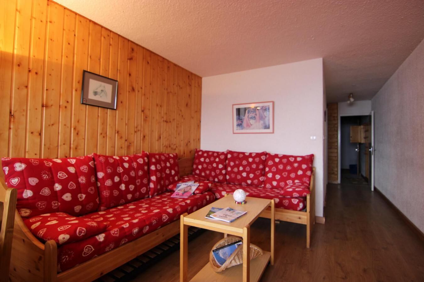 A cozy living room with a red patterned sofa, a wooden coffee table, and a framed picture on the wall.
