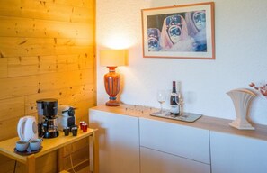 Una cocina con cafetera, tazas, una botella de vino y vasos sobre la encimera.