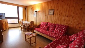A cozy living room with a red patterned sofa, a wooden coffee table, and a dining area with a table and chairs. - 200m from ski slopes, 1st floor, balcony, tv, 37m², Val Thorens (Val Thorens)