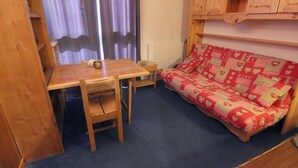 A small room with a wooden table and chairs, a red patterned sofa, and a wooden cabinet above the sofa. - 200m from ski slopes, 4th floor, tv, 18m², Val Thorens (Val Thorens)