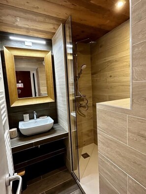 A bathroom with a glass-enclosed shower, a sink with a mirror above it, and wooden wall panels.