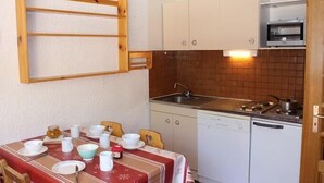 Eine kompakte Küche mit Spüle, Herd und kleinem Backofen. Ein Esstisch ist mit Tellern und Tassen gedeckt.