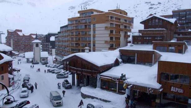 Een besneeuwde stad met meerlaags gebouwen, een centrale toren en geparkeerde auto's.