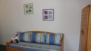 Een houten bank met gestreepte kussens en een tijdschrift erop. Twee ingelijste foto's hangen aan de muur.