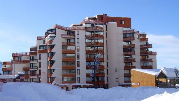 Monikerroksinen hotelli, jossa on parvekkeet, hiihtohissi ja puinen rakennelma, jonka kyltissä lukee ”SKISET”.