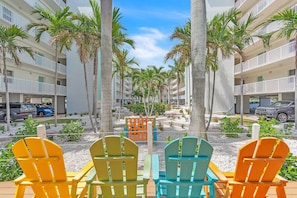 A row of colorful Adirondack chairs facing a building with balconies and palm trees. - Sunset Vistas 211N- Beachfront, Great amenities! (Treasure Island)