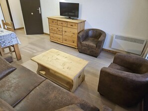 Uma sala de estar com uma mesa de centro de madeira, dois sofás castanhos, um armário de madeira com uma televisão e um radiador.