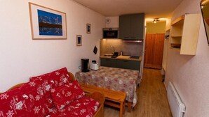 Ein kleines Zimmer mit Küchenzeile, einem Esstisch, einem roten Sofa und einem gerahmten Bild an der Wand.