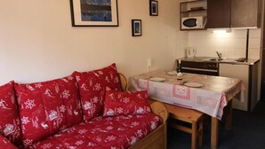 Ein gemütliches Wohnzimmer mit einem roten Sofa und einem Esstisch für zwei Personen.