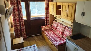 Eine kleine Küche mit Holzschränken, einer eingebauten Sitzbank mit gemusterten Kissen und einem Fenster mit Vorhängen.