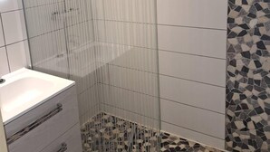 Un baño con cabina de ducha de vidrio, un lavabo blanco y suelo de baldosas.
