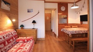 Una habitación acogedora con una cama de madera, una mesita con una lámpara, una mesa de comedor con sillas, un reloj en la pared y un televisor sobre la mesa de comedor.