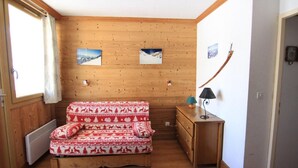 Una habitación acogedora con pared de madera, una cama con manta estampada, un pequeño aparador de madera y una lámpara.