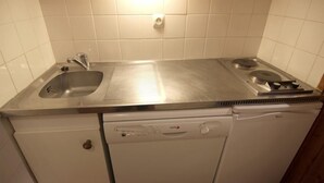 Una cocina compacta con encimera de acero inoxidable, un lavabo, lavavajillas y estufa.