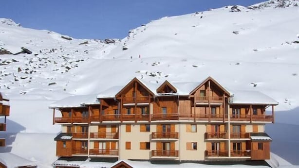 A multi-story wooden lodge with balconies, set against a snowy mountain backdrop.