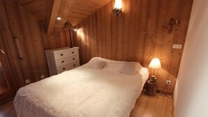 A cozy wooden room with a bed, a dresser, and a lamp.