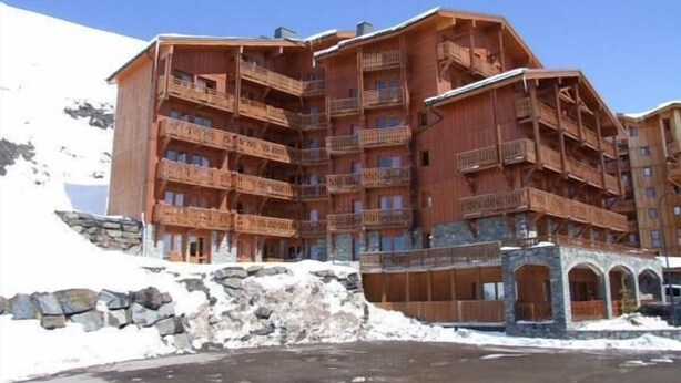 Un edificio in legno a più piani con balconi, un muro in pietra e terreno innevato.