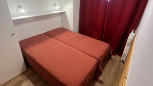 Un piccolo alloggio con una sola stanza, dotato di un letto, uno specchio, uno scaffale e una finestra con tende rosse.