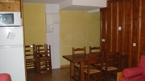 Un ambiente compatto con angolo cottura, un tavolo da pranzo con sedie e un divano rosso.