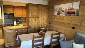 A cozy kitchen with wooden cabinets, a dining table with chairs, and a painting of a ski lift on the wall. - 3rd floor, balcony, tv, ski locker, 56m², Val Thorens (Val Thorens)