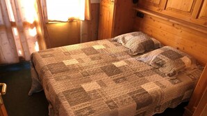 A cozy room with a bed covered in a patterned quilt, wooden walls, and a door to the left. - 3rd floor, balcony, tv, ski locker, 56m², Val Thorens (Val Thorens)