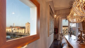 A narrow hallway with a large window overlooking a cityscape, a chandelier, and a table with decorative items. - Superior room with balcony overlooking the canal port of Cesenatico (Cesenatico)