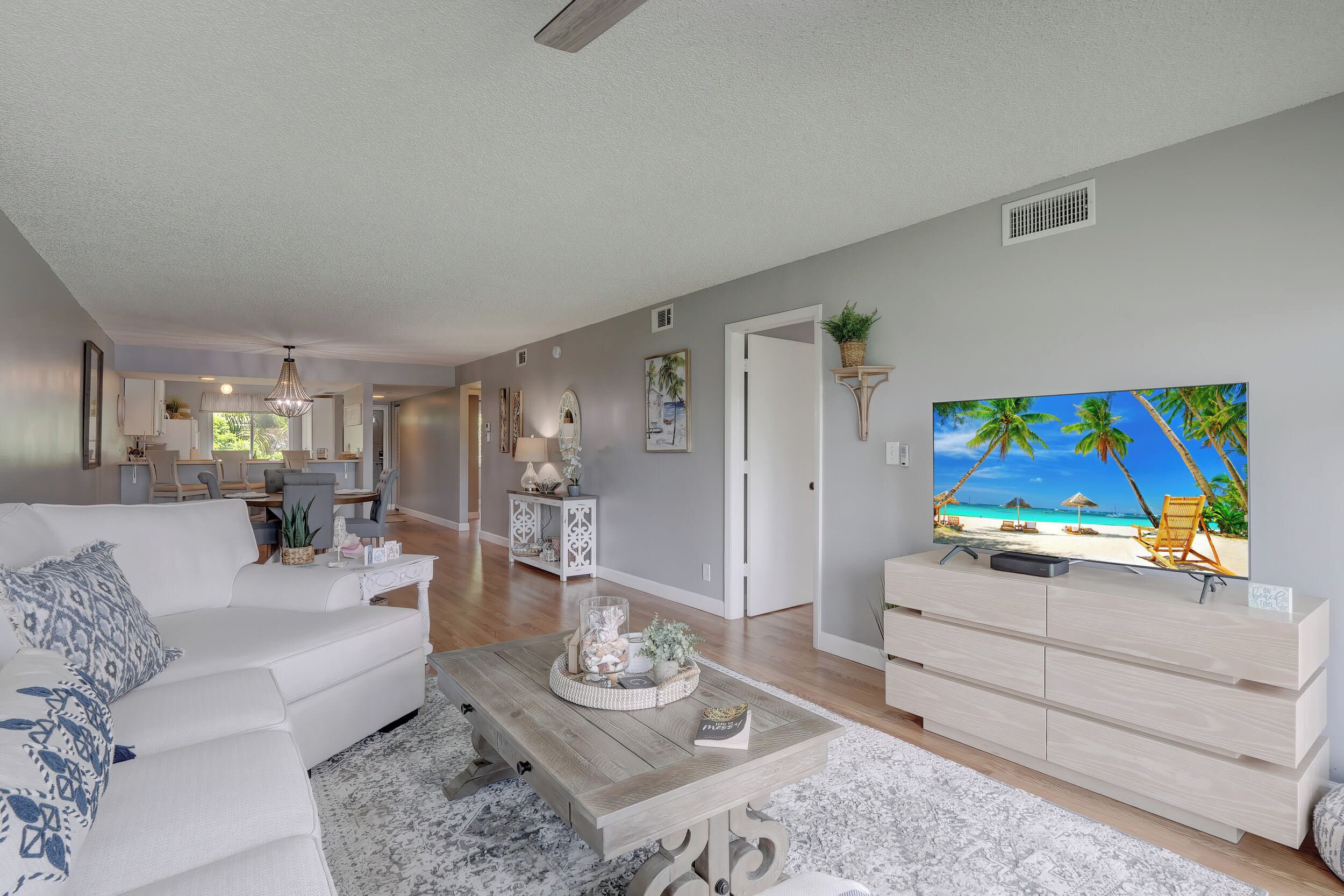 Una sala de estar con televisor, sofá, mesa de centro y una cocina al fondo.