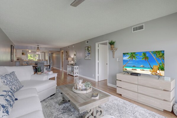 A living room with a television, a sofa, a coffee table, and a kitchen in the background.