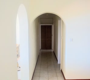 Un couloir étroit, dont le sol est recouvert de carreaux, mène à une porte au fond.