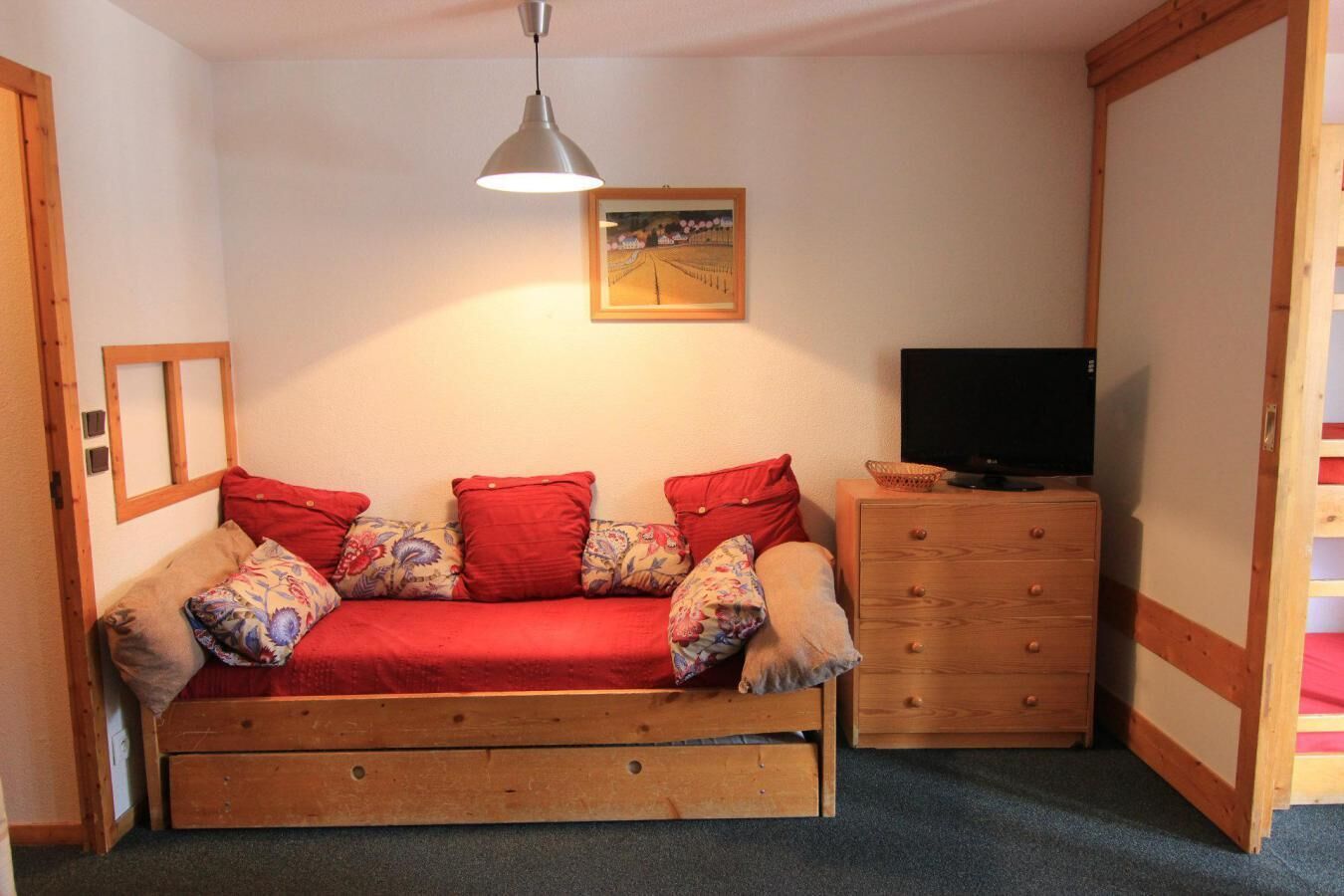Ein gemütliches Zimmer mit einer Holz-Couch, einer Holzkommode, einem Fernseher und einem gerahmten Bild an der Wand.