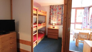 A room with bunk beds, a desk with a lamp, a television, and a window with floral curtains. - 50m from ski slopes, 2nd floor, balcony, tv, 35m², Val Thorens (Val Thorens)