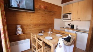 A wooden interior with a dining table set for four, a television mounted on the wall, and a kitchen area with a microwave and refrigerator.