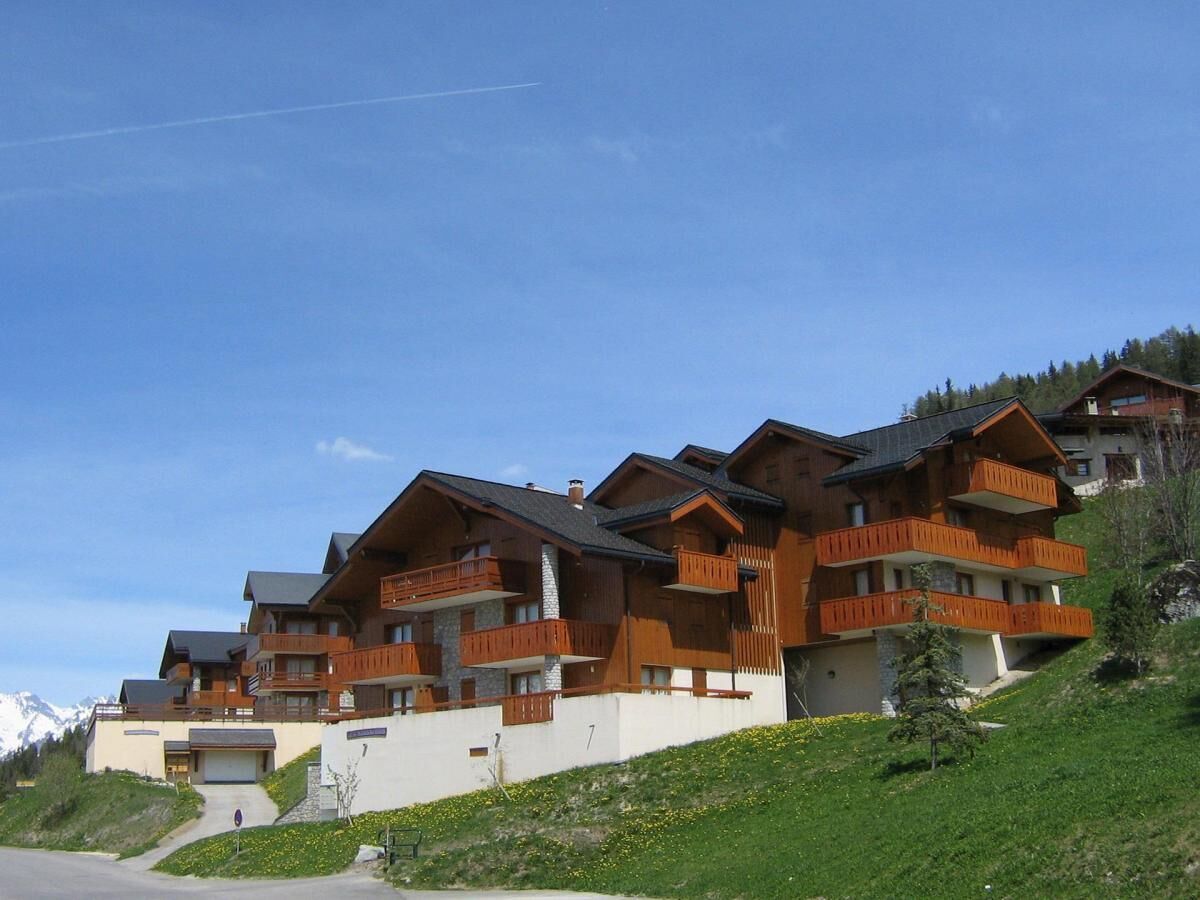 Une rangée de bâtiments en bois de style chalet, dotés de balcons, se dressant sur un fond de montagnes.