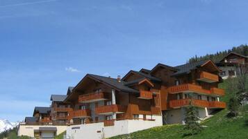 Une rangée de bâtiments en bois de style chalet, dotés de balcons, se dressant sur un fond de montagnes.