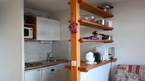 A compact kitchen with white cabinets, a microwave, a stove, and a coffee maker on a wooden shelf. - 150m from ski slopes, 1st floor, tv, ski locker, 52m², Peisey-Vallandry (Landry)