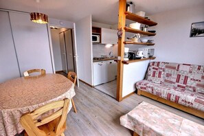 A compact living space with a dining table, a sofa, a kitchenette, and a wooden shelf unit. - 150m from ski slopes, 1st floor, tv, ski locker, 52m², Peisey-Vallandry (Landry)
