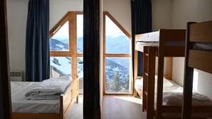 A room with two wooden bunk beds and a single bed, large windows with curtains, and a view of mountains. - 150m from ski slopes, 1st floor, tv, ski locker, 52m², Peisey-Vallandry (Landry)