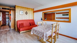 A cozy room with a wooden floor, a red sofa, a dining table with chairs, and a mirror on the wall. - 150m from resort center, 1st floor, balcony, parking, tv, 35m², Les Arcs (Bourg-Saint-Maurice)
