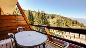 A wooden deck with a table and chairs, overlooking a forested mountain area. - 150m from resort center, 1st floor, balcony, parking, tv, 35m², Les Arcs (Bourg-Saint-Maurice)