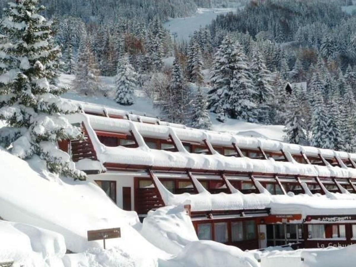 A snow-covered lodge with multiple levels, surrounded by a forested mountain area.