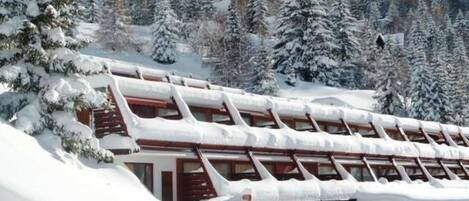 A snow-covered lodge with multiple levels, surrounded by a forested mountain area.