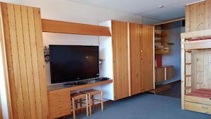 Een kamer met een televisie, houten meubels en een stapelbed.