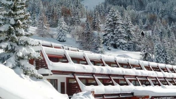 Een met sneeuw bedekte lodge met een schuin dak en meerdere ramen, omgeven door een besneeuwd bos.