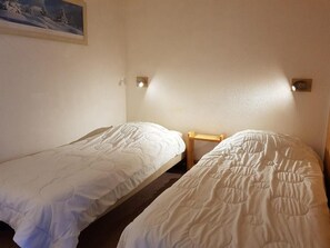 Two single beds with white duvets and pillows, a framed picture, and a wooden bench.