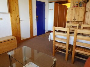 Una habitación con una mesa de madera, sillas, una puerta azul y un armario de madera con utensilios de cocina.
