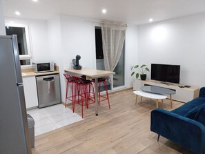 A compact living space with a kitchenette, a dining area with red chairs, a TV, and a blue sofa.